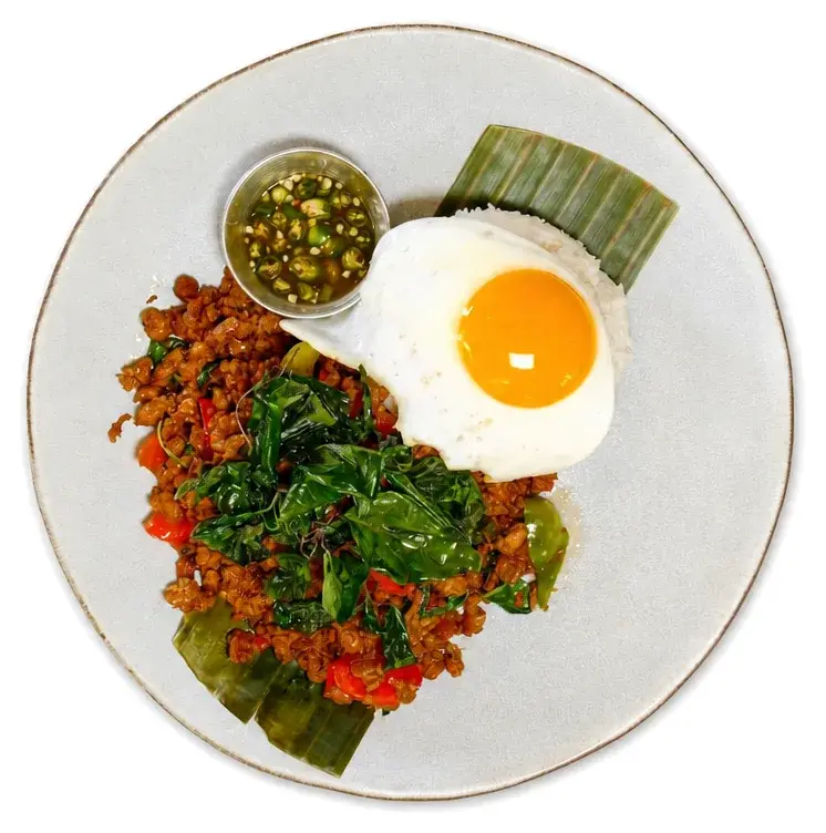 Minced meat with Thai basil, a fried egg and a pot of green chilli sauce on a banana leaf