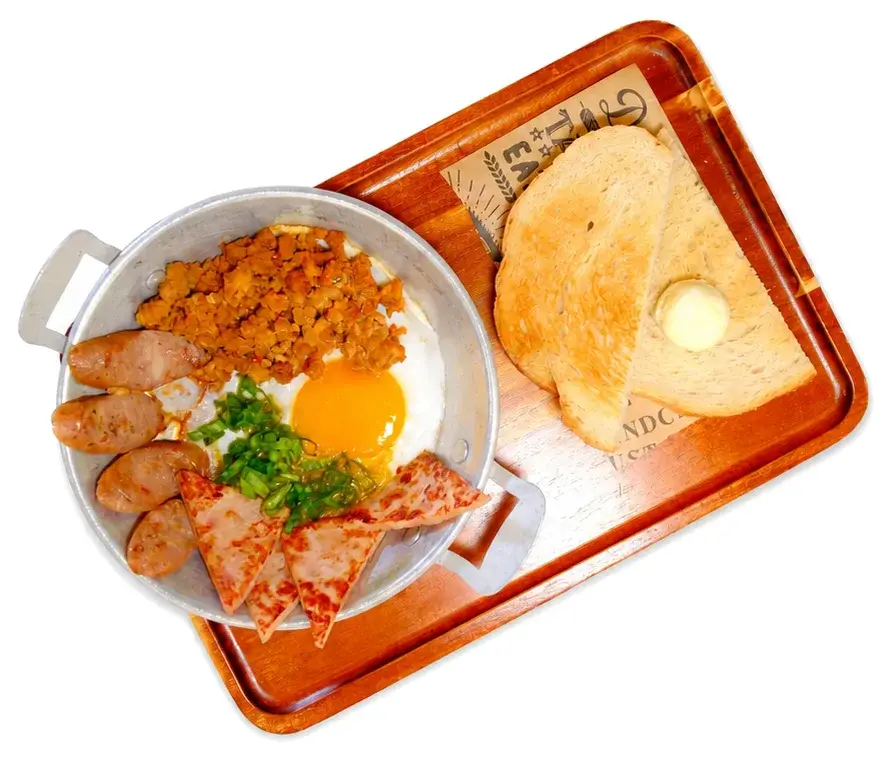 A skillet of sausage and fried egg with toast on a copper tray